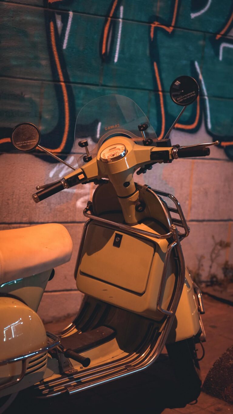 A classic scooter parked by a vibrant graffiti wall at night, showcasing urban charm.